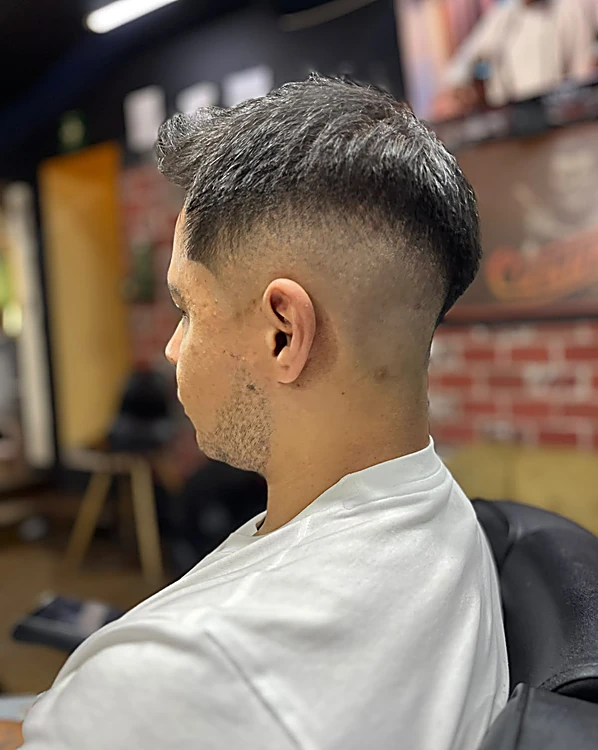 Fade bajo de perfil con el cabello texturizado arriba y la línea del degradado marcada sobre la oreja