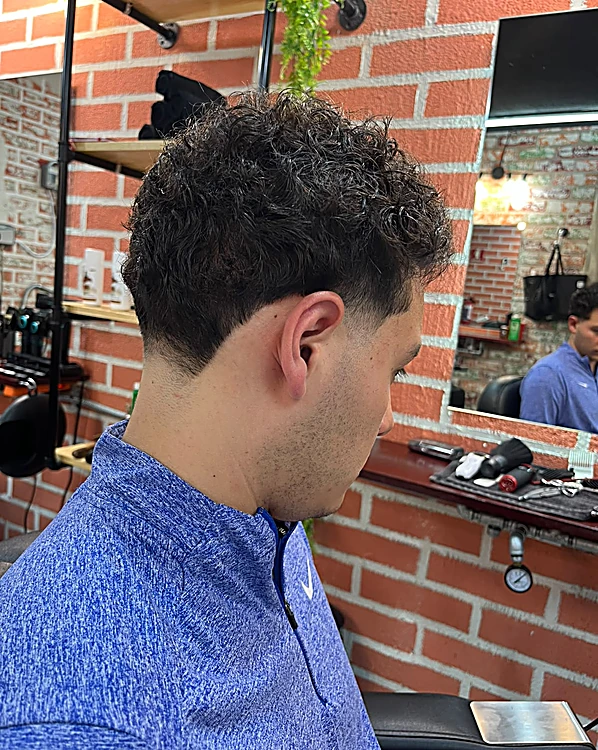 Cabello rizado texturizado arriba con degradado a los lados, de perfil frente al espejo