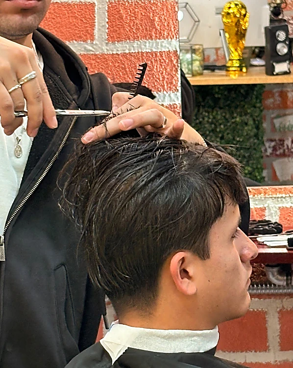 Manos con tijera y peine trabajando el flequillo de un cliente, con anillos en los dedos del barbero